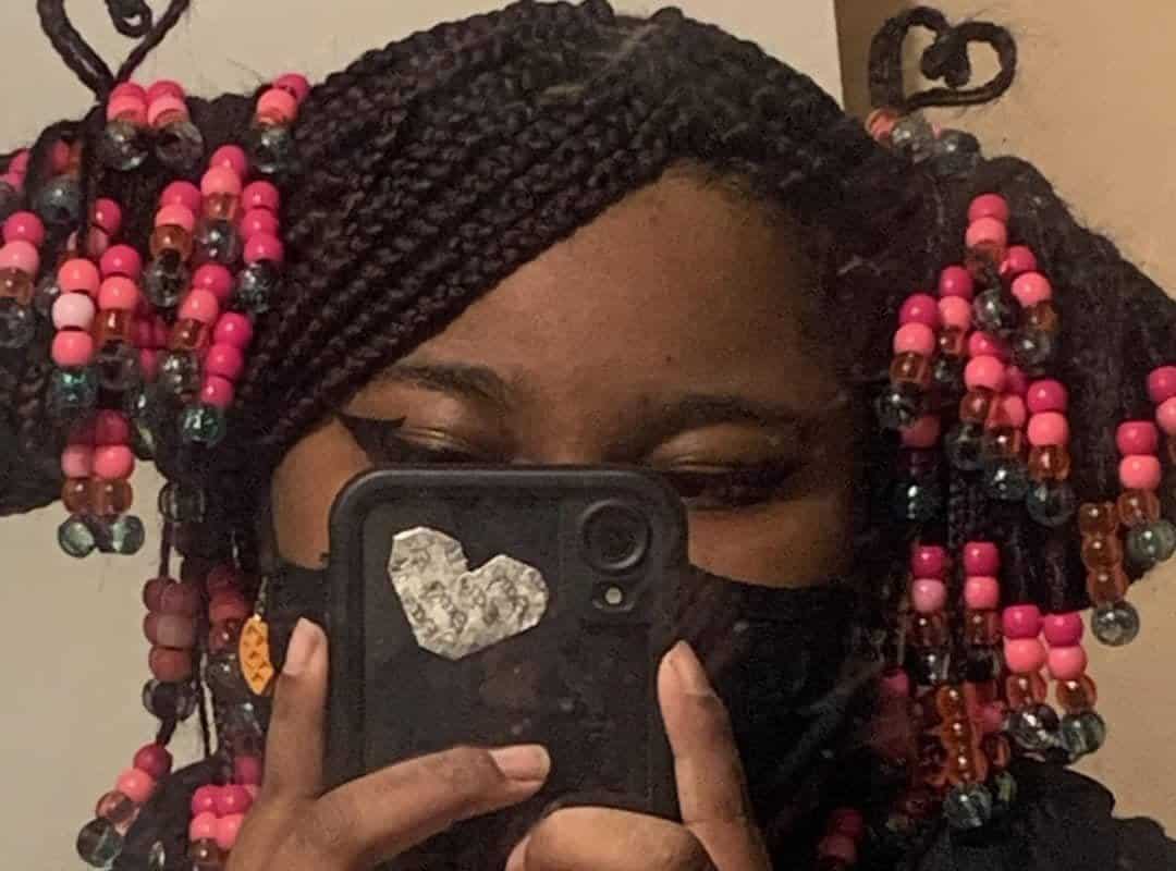 girl with black box tribal braids in bun with colored beads and phone